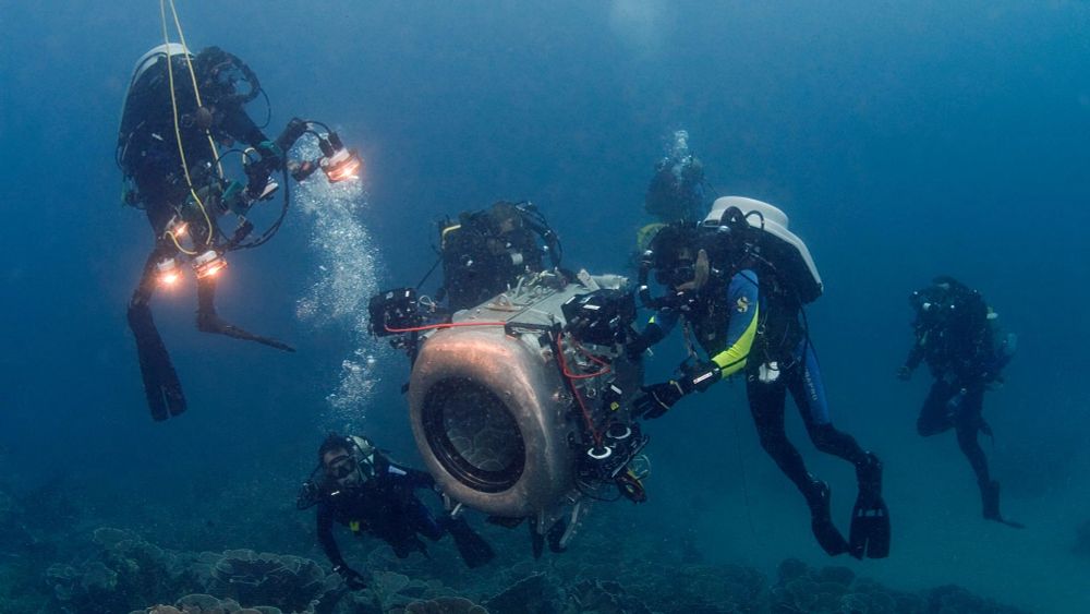 Team of scuba divers positioning large camera near ocean floor