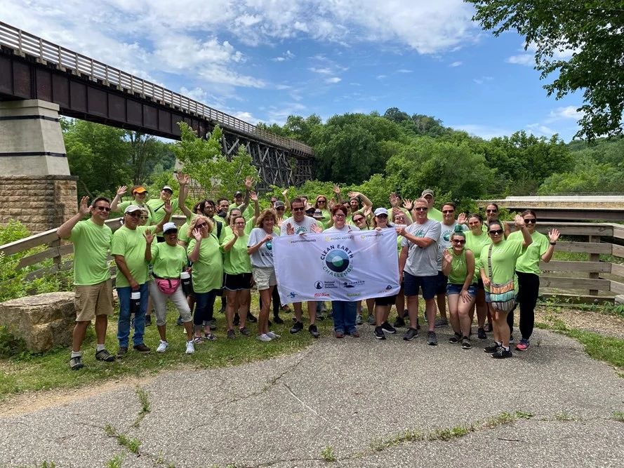 Minn Kota employees holding Clean Earth Challenge banner in front of bridge
