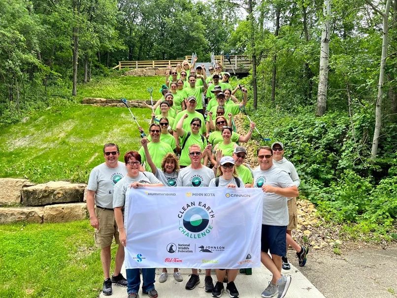Minn Kota employees lined up with Clean Earth Challenge banner and trash pickup sticks