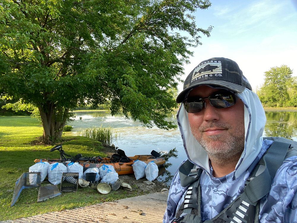 Old Town fisherman with multiple trash bags full of trash by lake